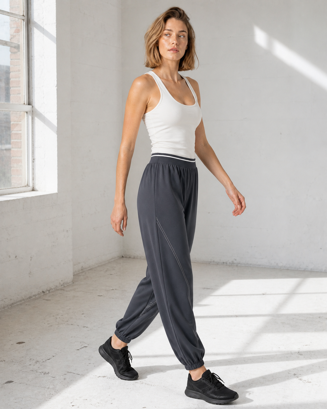 Model stepping through a bright studio in deep Grey relaxed joggers.