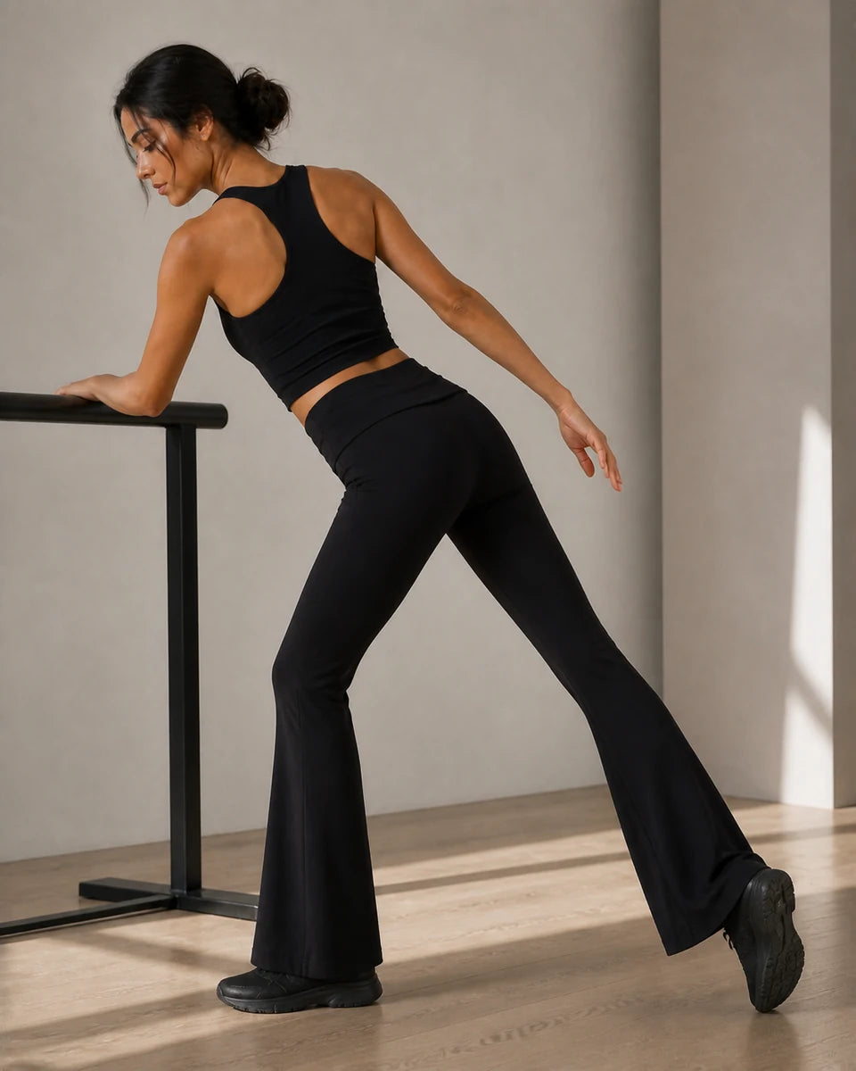 Model showing the rear and side fit of Black Foldover Flare Pilates Pants at a studio barre